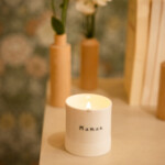 Bougie artisanale allumée dans un contenant en porcelaine blanche avec l’inscription “Maman”.